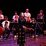 A singer performs at a microphone with a band in the background